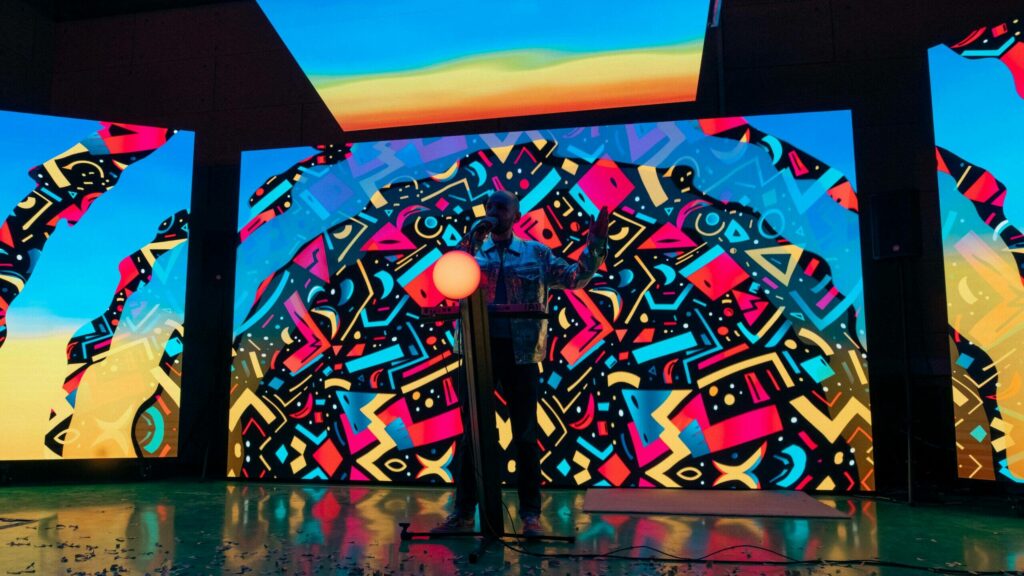 Le mur LED du plateau affichant un décor graphique aux couleurs vives, une silhouette seule au centre du plateau
